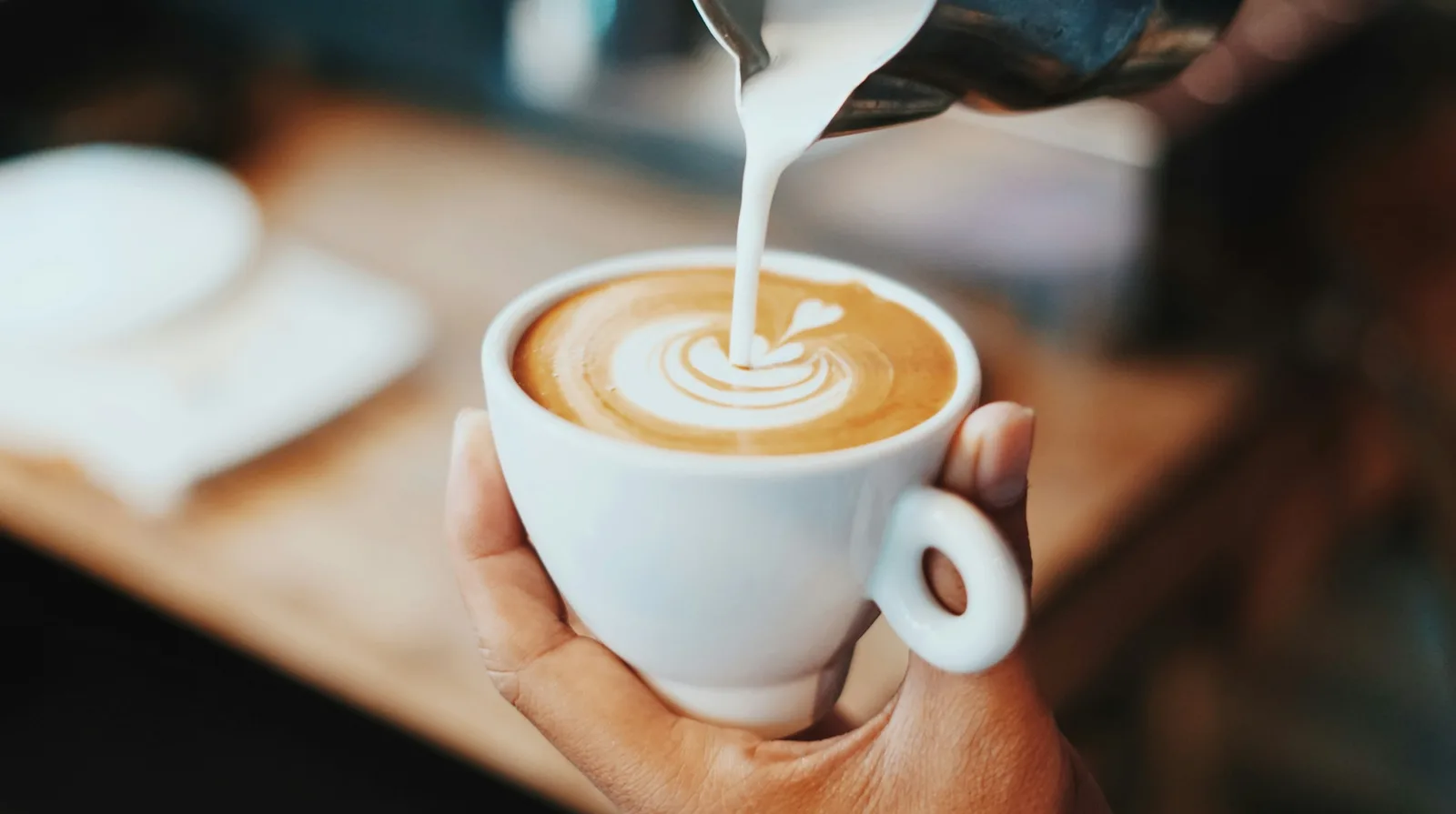 Steamed milk poured into a latte held in one hand, the leaf pattern taking shape.