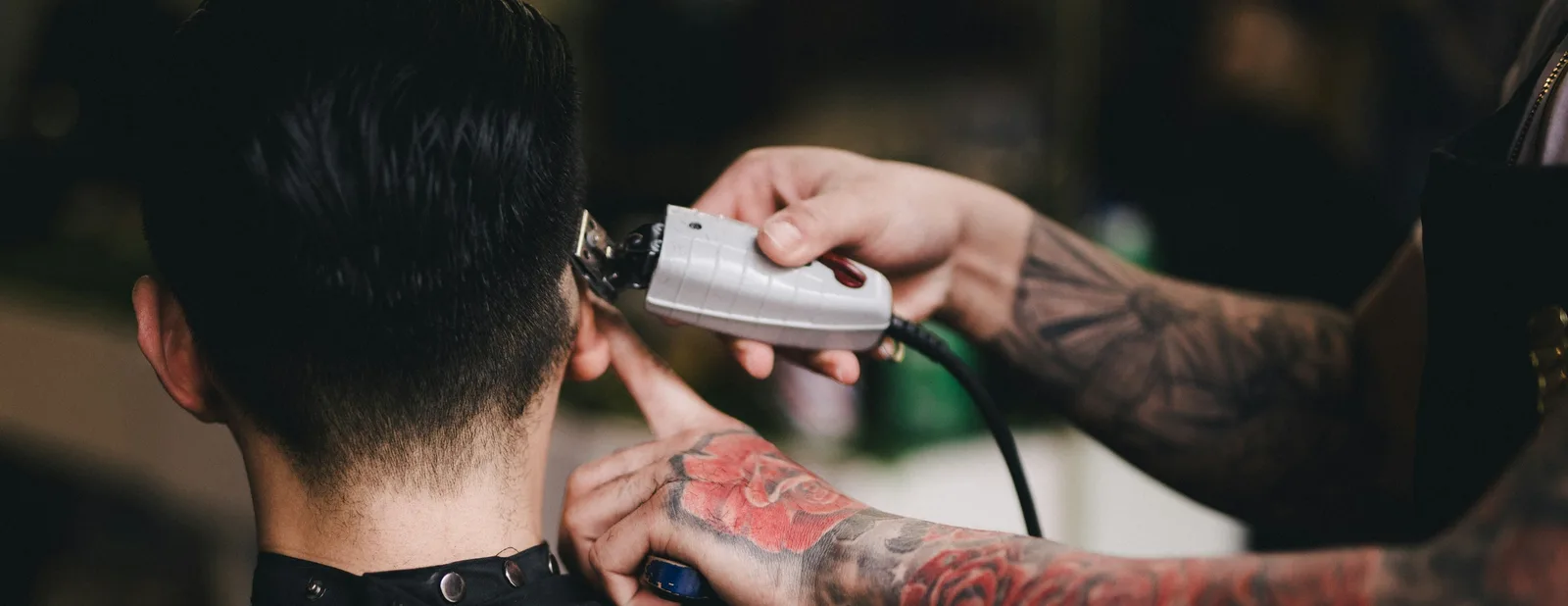 A clipper cut seen from behind, the barber's tattooed hands tidying the neckline.