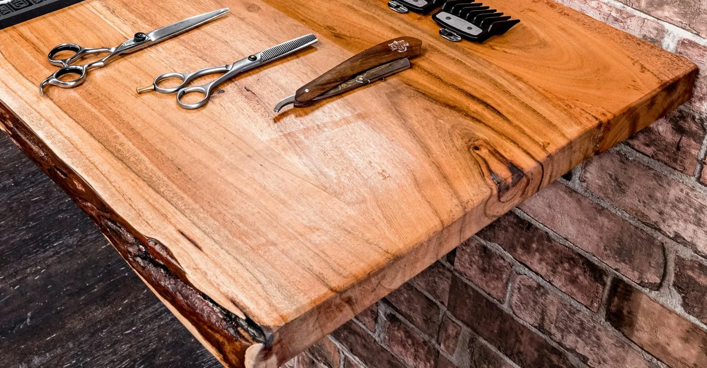 Two pairs of shears and a straight razor laid out on a live-edge wooden counter against brick.