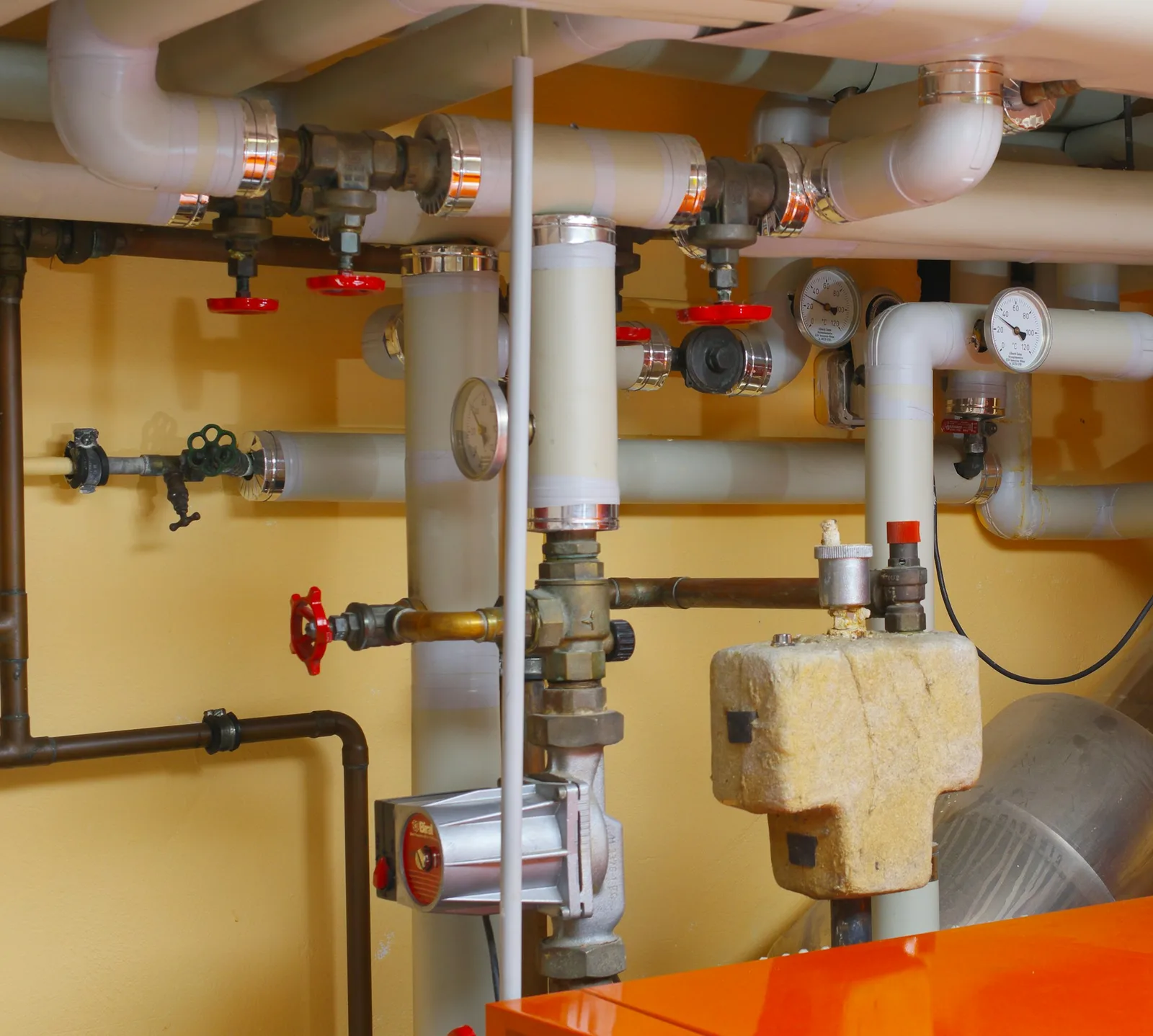 Insulated pipes, red valve wheels and pressure gauges running above an orange boiler.