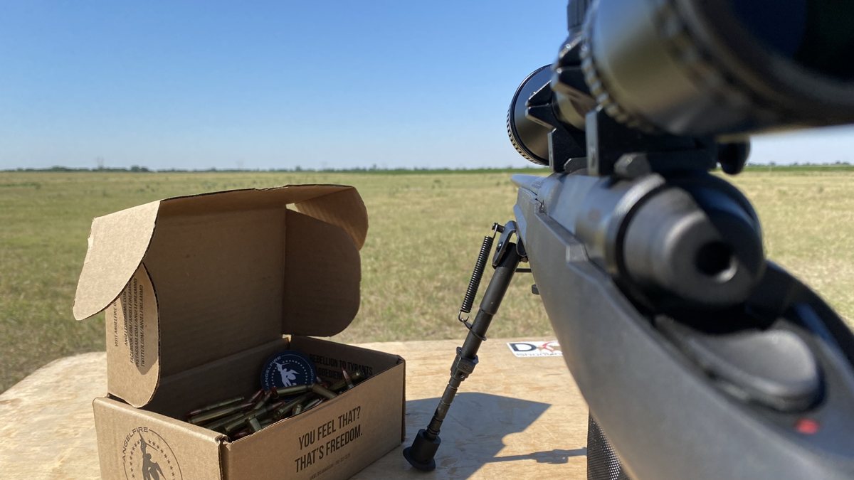 An open AngelFire box of ammunition on a range bench beside a scoped rifle.