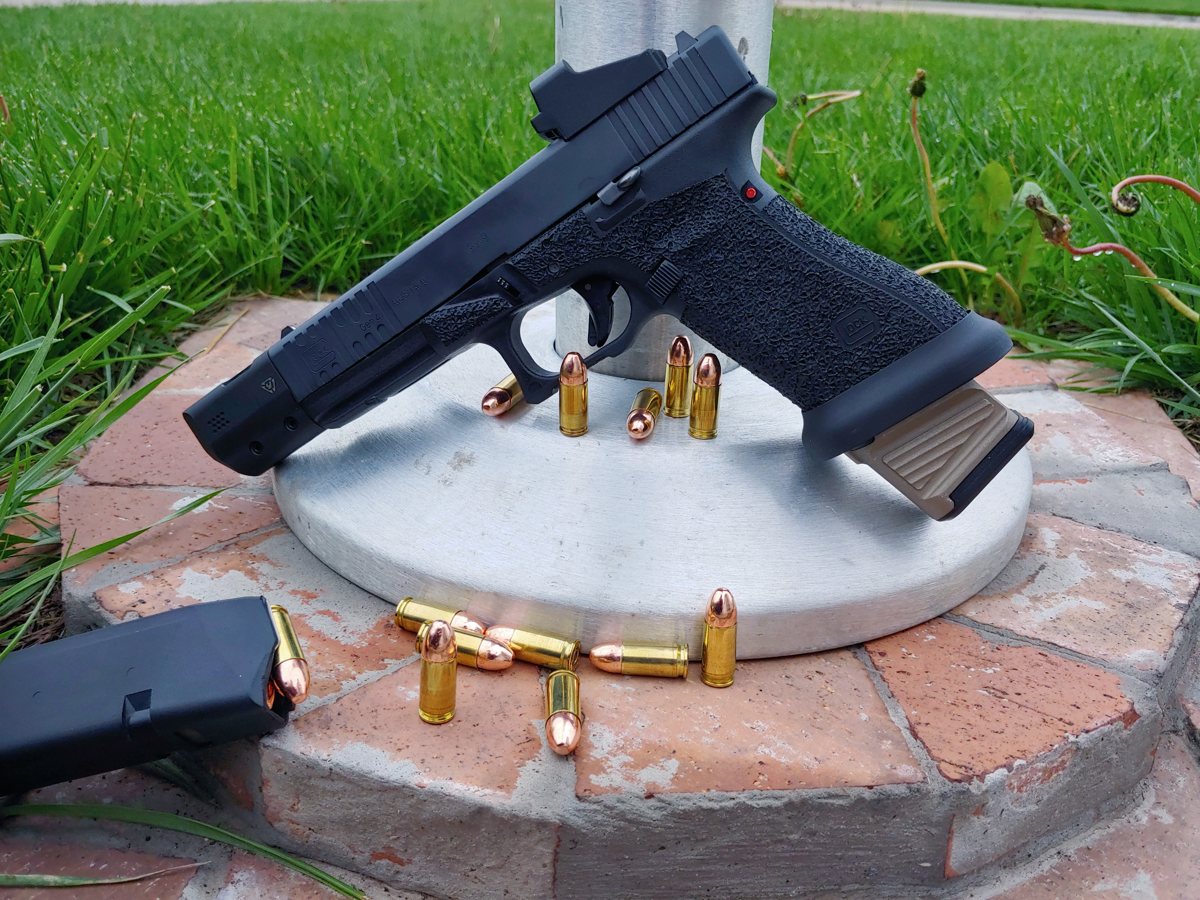 A handgun with a red dot sight and loose 9mm rounds on a brick ledge.